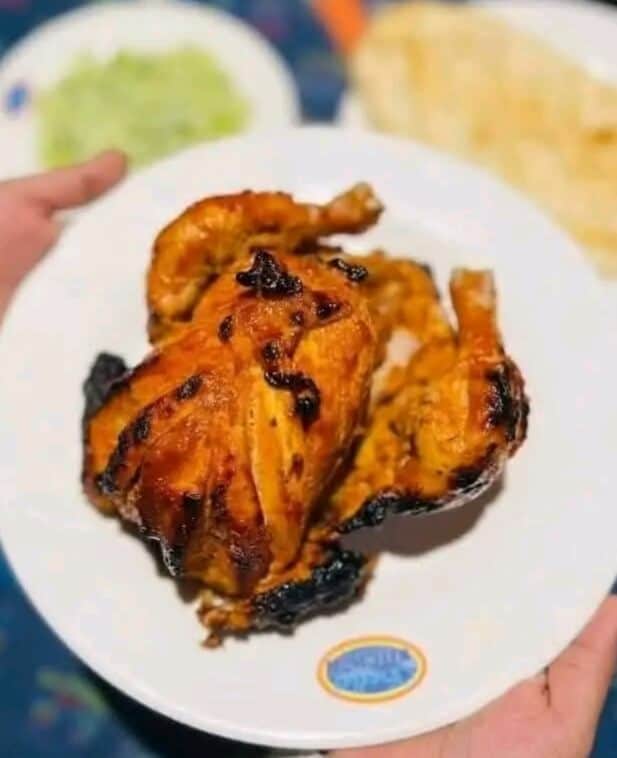A whole, grilled chicken from Sadia's Kitchen, showcasing the golden-brown skin, perfect char marks, and juicy appearance. The chicken is presented on a platter, ready to be served.