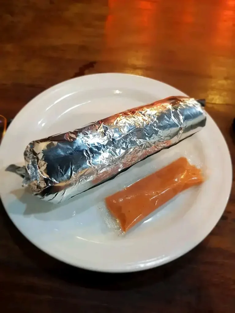 Sadia's Kitchen chicken shawarma, wrapped in foil and served on a white plate with a small packet of their signature homemade tomato sauce.